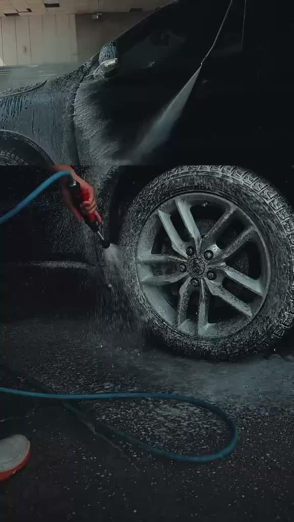 A black car covered in cleaning foam, a pressure-washer lance held to the front wheel arch